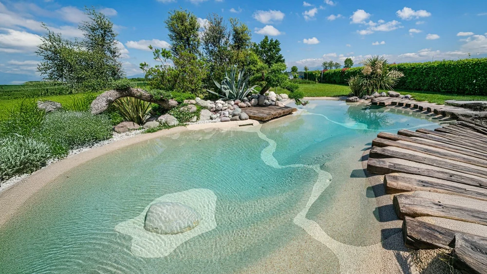 Piscine extérieure avec escalier immergé en pierre naturelle, entourée de végétation méditerranéenne incluant palmiers et lauriers-roses en fleurs