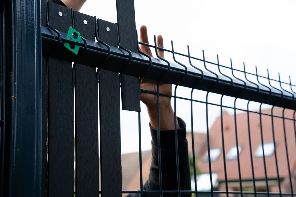 Entrée résidentielle avec portail métallique automatisé noir à deux vantaux, piliers en béton blanc, interphone intégré