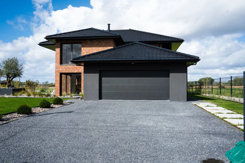 Rue résidentielle avec revêtement d'asphalte fraîchement posé, bordée de maisons unifamiliales avec garages et jardins paysagers