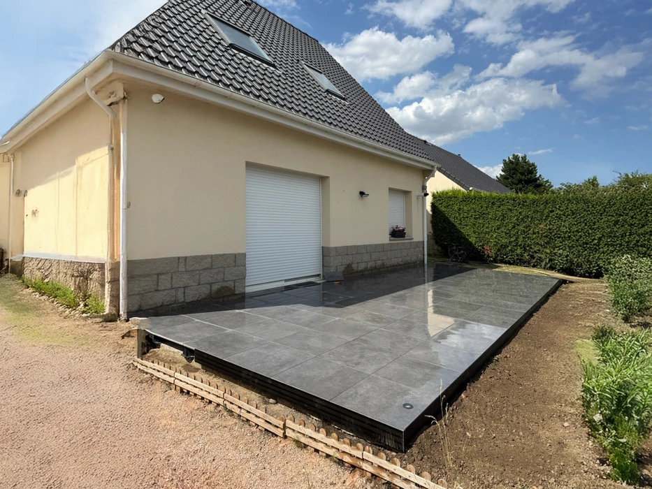 Maison moderne avec panneaux solaires photovoltaïques installés sur toiture tuiles noires, façade blanche contemporaine, garage ouvert avec vélo, éclairage LED extérieur, jardin paysager