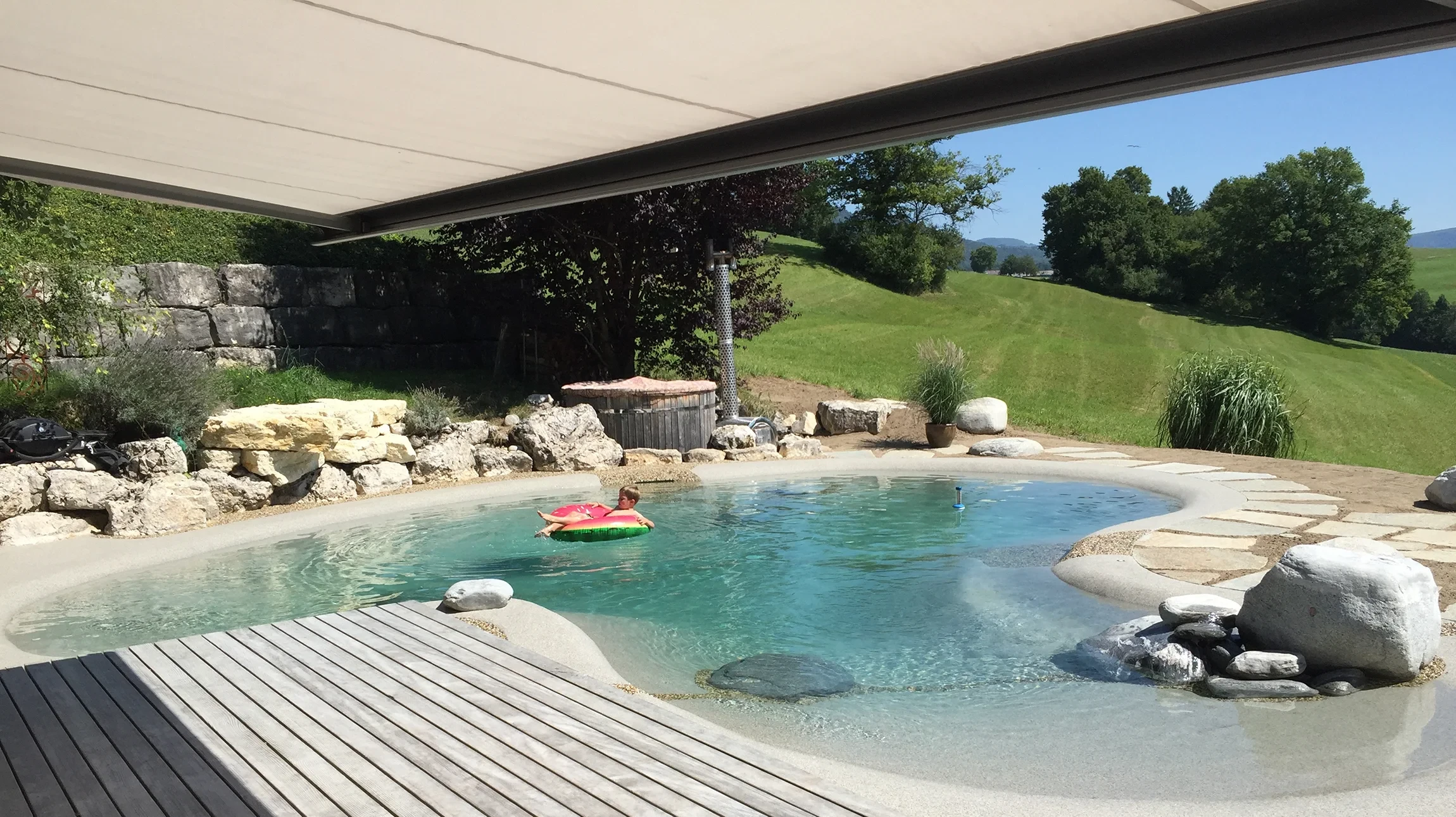 Jardin aquatique extérieur avec bassin d'ornement, jet d'eau décoratif en arc provenant d'une sculpture ornementale posée sur enrochement naturel